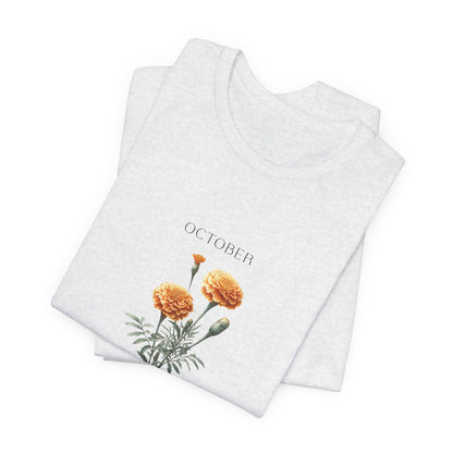 A t-shirt featuring a beautiful marigold for October with traits Passion, Creativity, Courage. Perfect for October birthdays and floral art lovers. Comfortable and stylish for casual outings or celebrations. Bella+Canvas 3001 t-shirt in ash. ReadyShirtAim.com