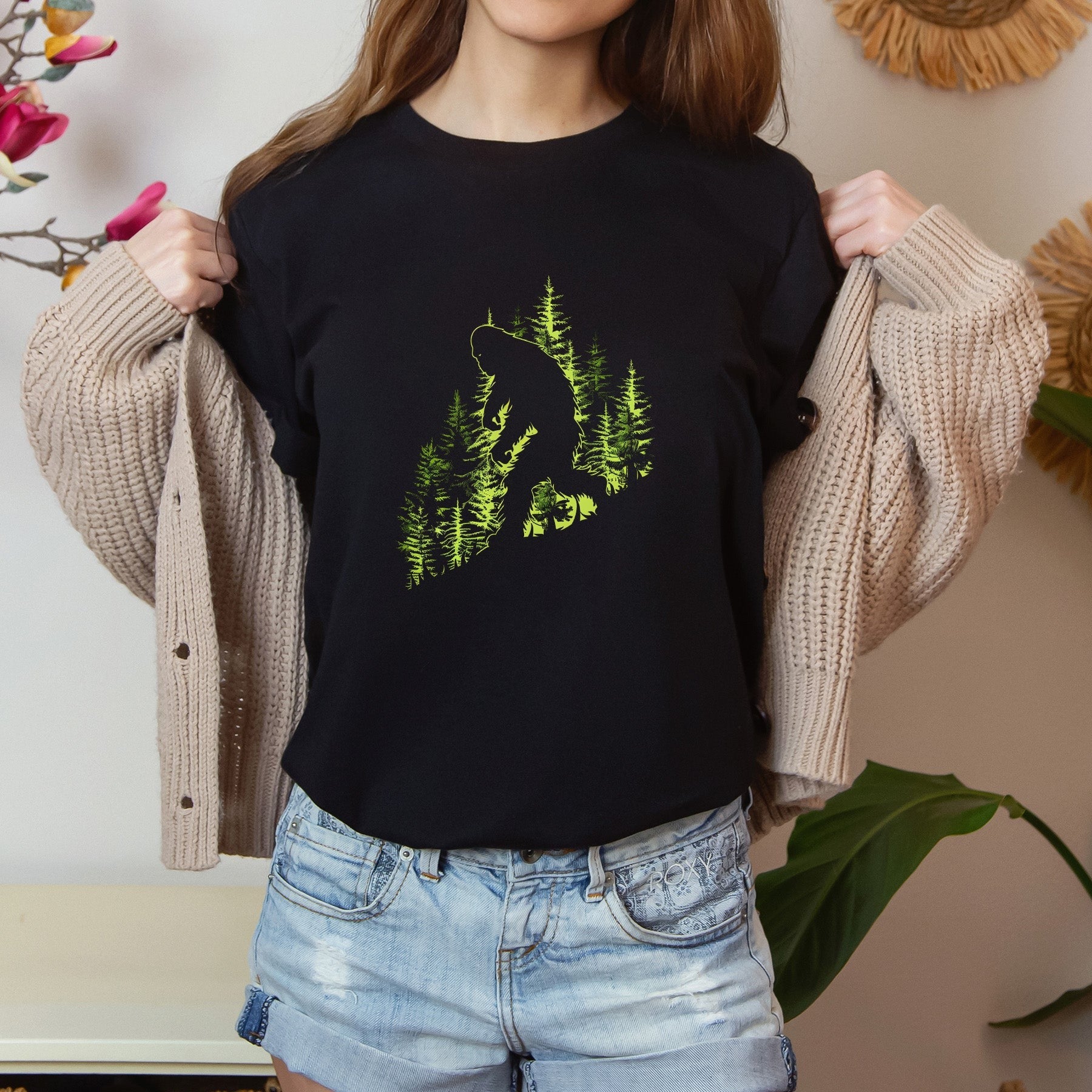 A t-shirt featuring an artistic depiction of a Bigfoot encounter, perfect for cryptid enthusiasts, outdoor adventurers, and mystery lovers. Comfortable and stylish for casual outings or cryptid conventions. Bella+Canvas 3001 t-shirt in black. ReadyShirtAim.com