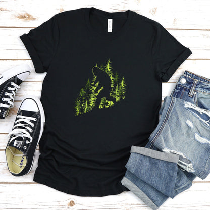 A t-shirt featuring an artistic depiction of a Bigfoot encounter, perfect for cryptid enthusiasts, outdoor adventurers, and mystery lovers. Comfortable and stylish for casual outings or cryptid conventions. Bella+Canvas 3001 t-shirt in black. ReadyShirtAim.com