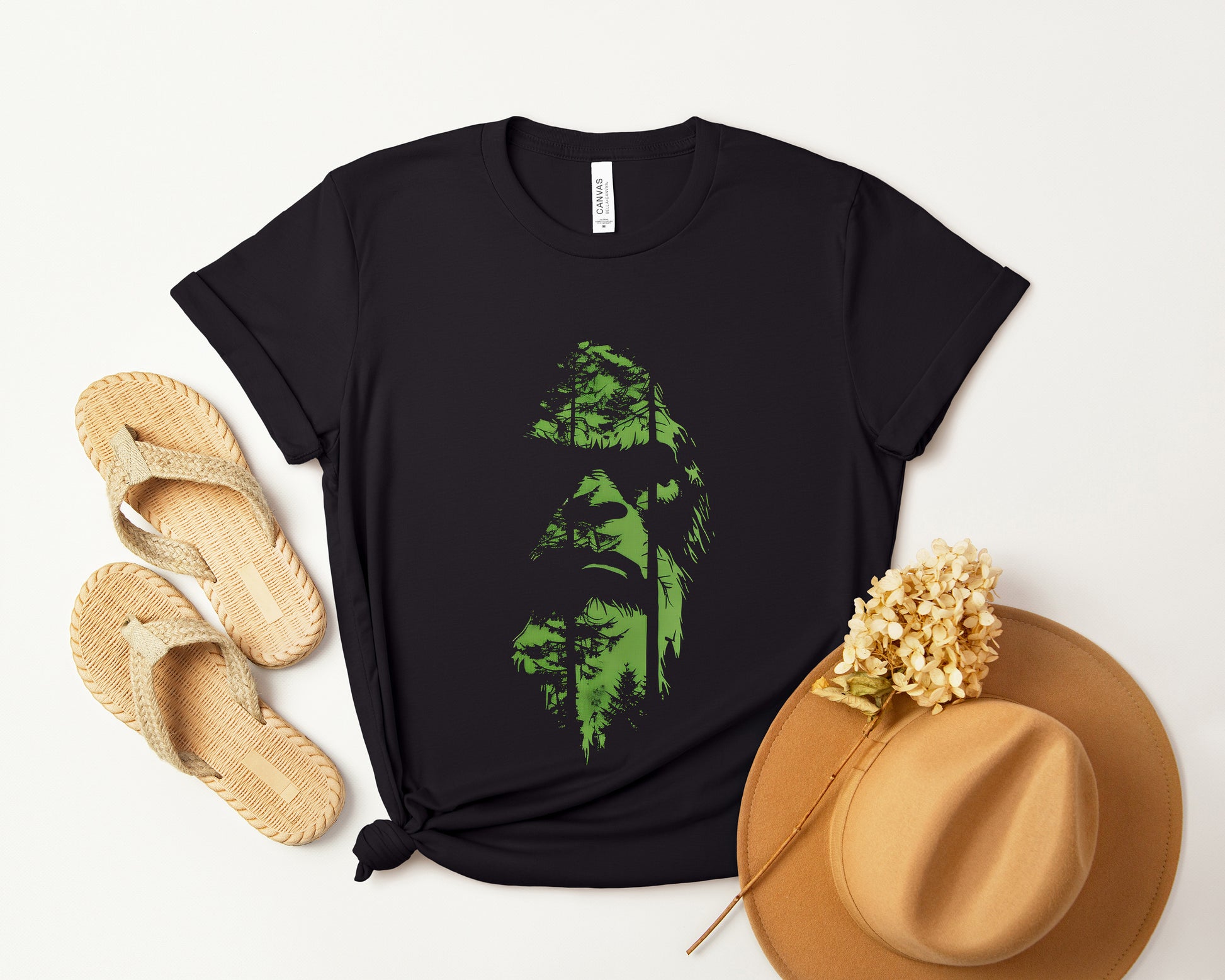 A t-shirt featuring an enigmatic cryptid design of Bigfoot's face, perfect for Bigfoot enthusiasts, cryptid fans, and adventure seekers. Comfortable and stylish for casual outings or cryptid conventions. Bella+Canvas 3001 t-shirt in black. ReadyShirtAim.com