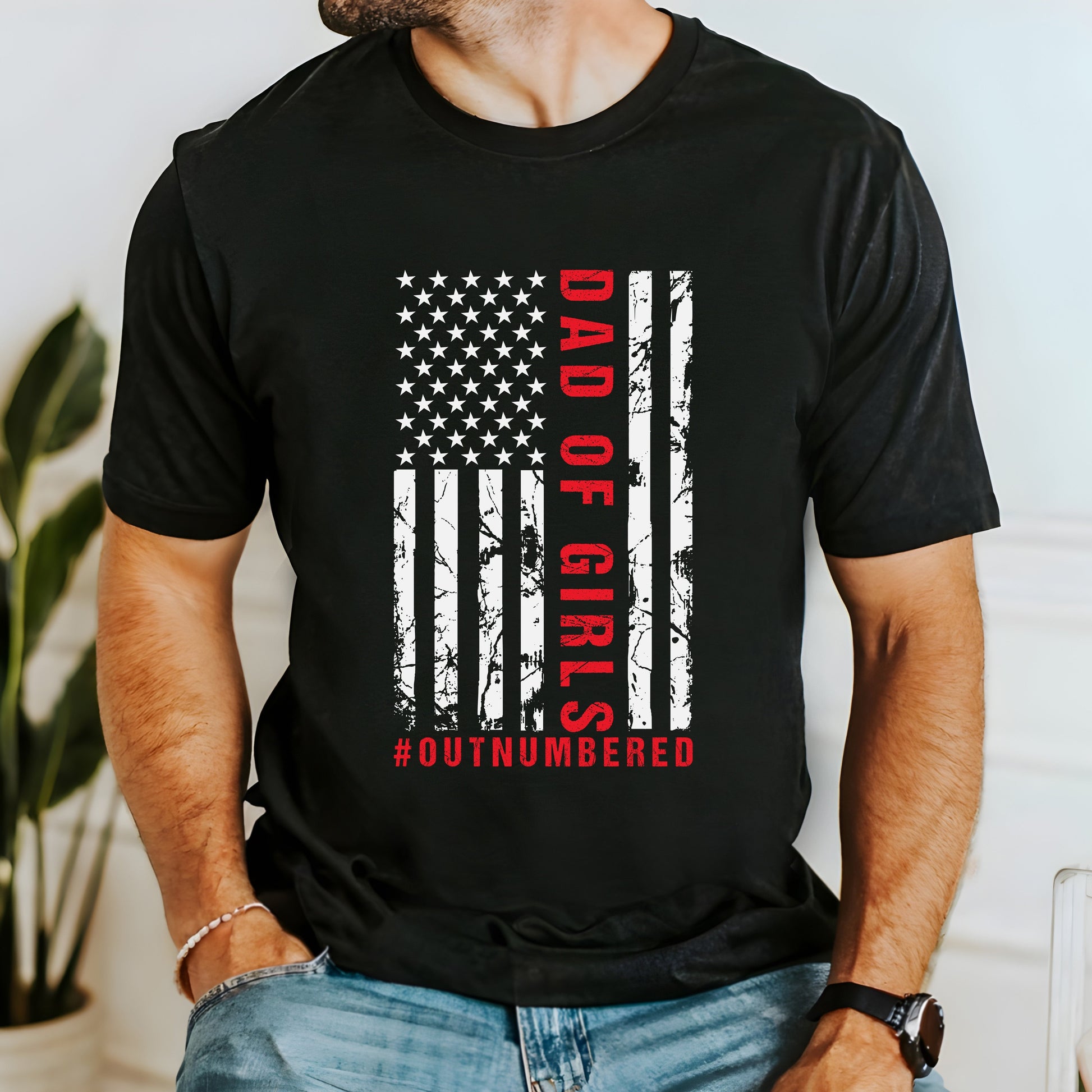 A dark-colored t-shirt featuring a grungy American flag design with the text "Dad of girls #outnumbered" in white and red. Perfect for Father's Day, Fourth of July, and patriotic dads who love humor. Comfortable and stylish for casual wear. Bella+Canvas 3001 t-shirt in black. ReadyShirtAim.com