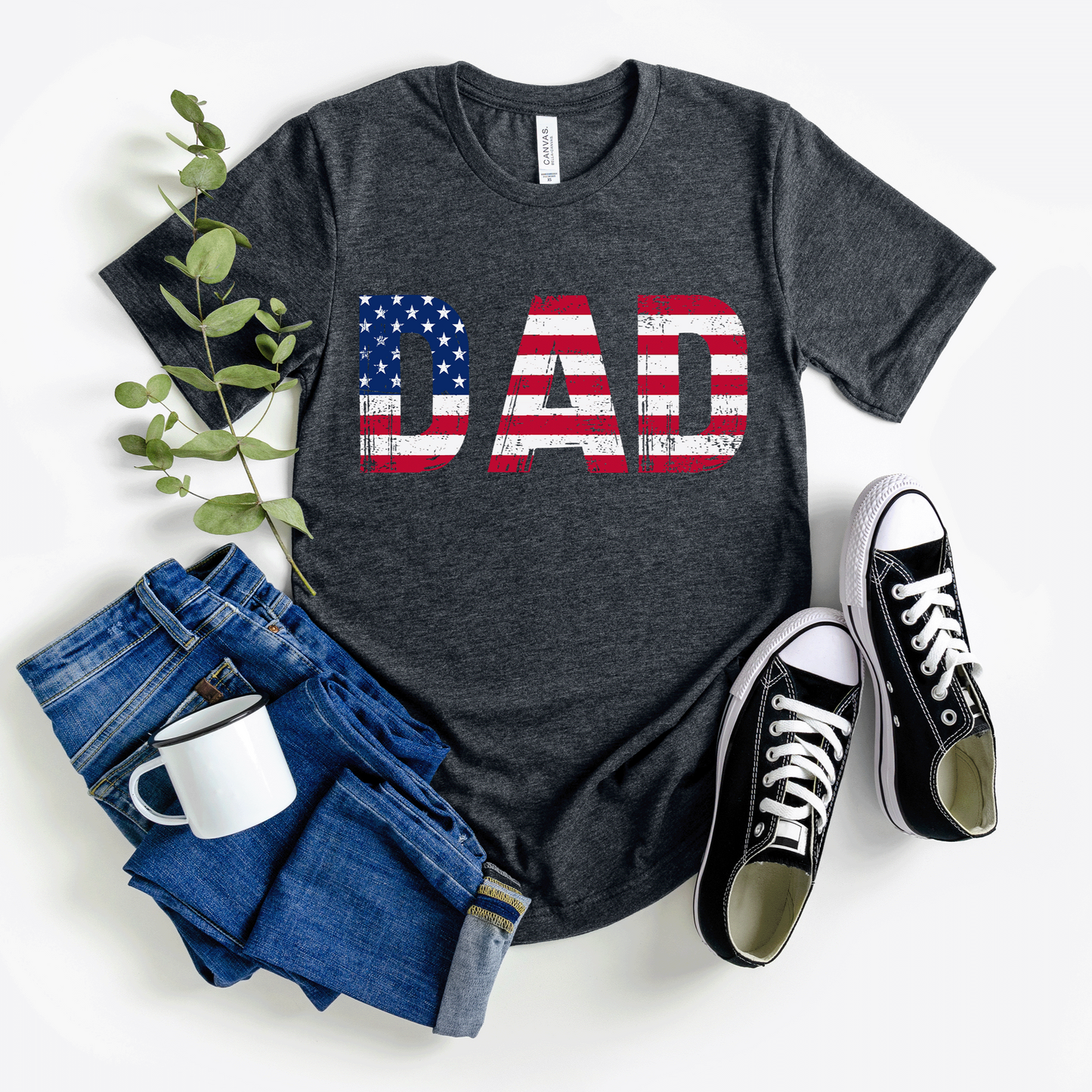 A dark t-shirt with bold "DAD" text filled with the American flag and a grunge texture. This patriotic shirt is perfect for Father's Day or any occasion to honor dad. Made from soft, breathable cotton for ultimate comfort. Available in multiple dark colors and sizes. Bella+Canvas 3001 t-shirt. ReadyShirtAim.com