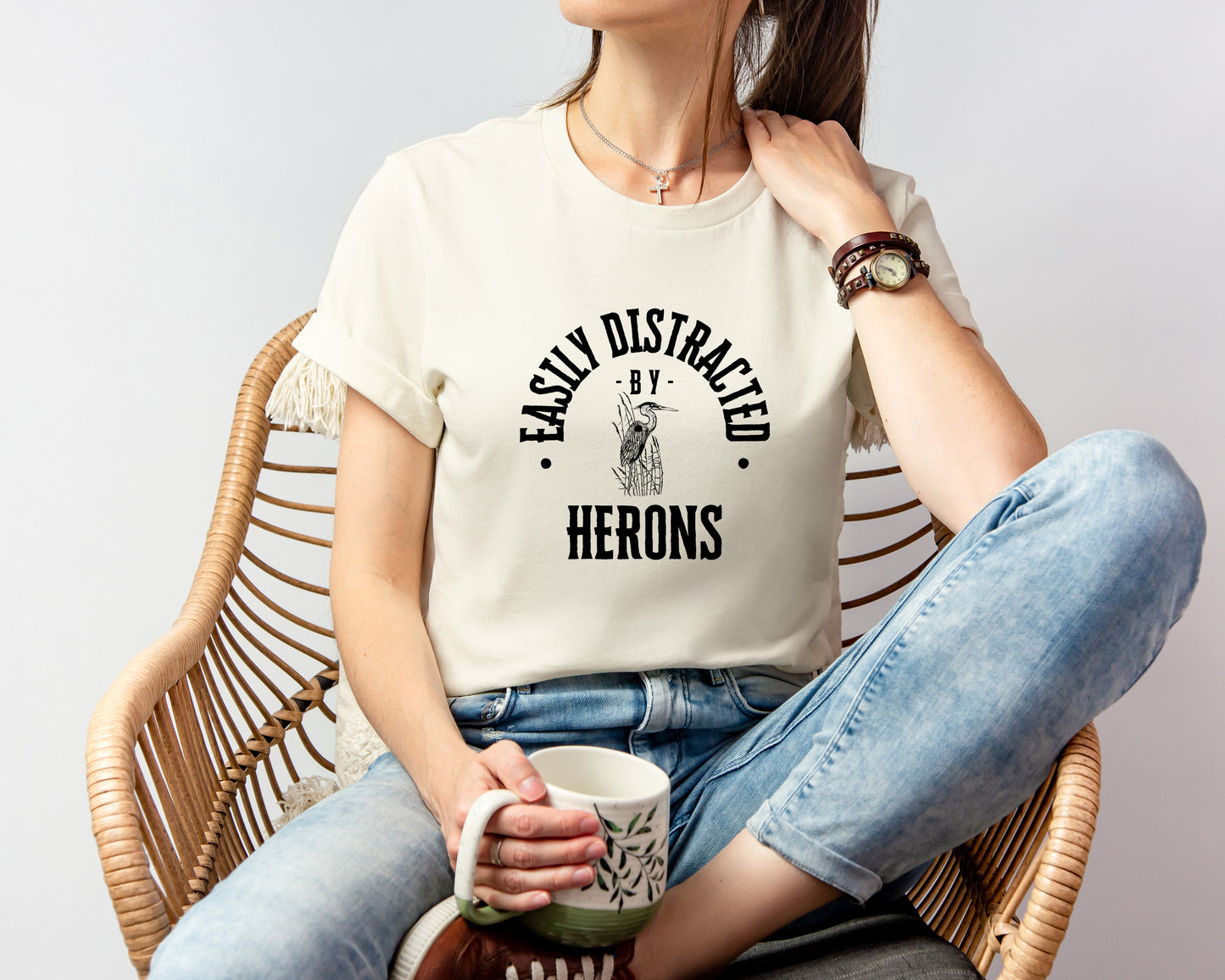 A vintage typeface t-shirt with a hand-drawn sketch of a heron and the caption "Easily Distracted by Herons." Perfect for heron lovers, bird watchers, and wildlife enthusiasts. Bella+Canvas 3001 t-shirt in natural. ReadyShirtAim.com