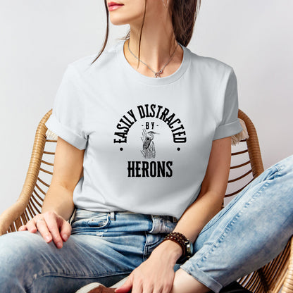 A vintage typeface t-shirt with a hand-drawn sketch of a heron and the caption "Easily Distracted by Herons." Perfect for heron lovers, bird watchers, and wildlife enthusiasts. Bella+Canvas 3001 t-shirt in silver. ReadyShirtAim.com