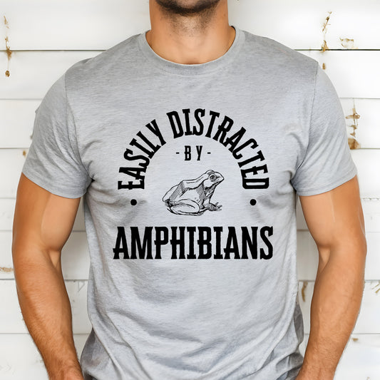 A vintage typeface t-shirt with a hand-drawn sketch of an amphibian and the caption "Easily Distracted by Amphibians." Perfect for amphibian lovers, herpetologists, and nature enthusiasts. Bella+Canvas 3001 t-shirt in athletic heather. ReadyShirtAim.com