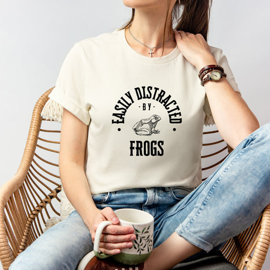 A vintage typeface t-shirt with a hand-drawn sketch of a frog and the caption "Easily Distracted by Frogs." Perfect for frog lovers, herpetologists, and nature enthusiasts. Bella+Canvas 3001 t-shirt in natural. ReadyShirtAim.com