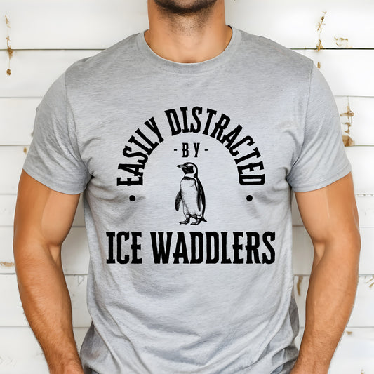 A vintage typeface t-shirt with a hand-drawn sketch of a penguin and the caption "Easily Distracted by Ice Waddlers." Perfect for penguin lovers, marine biologists, and wildlife enthusiasts. Bella+Canvas 3001 t-shirt in athletic heather. ReadyShirtAim.com