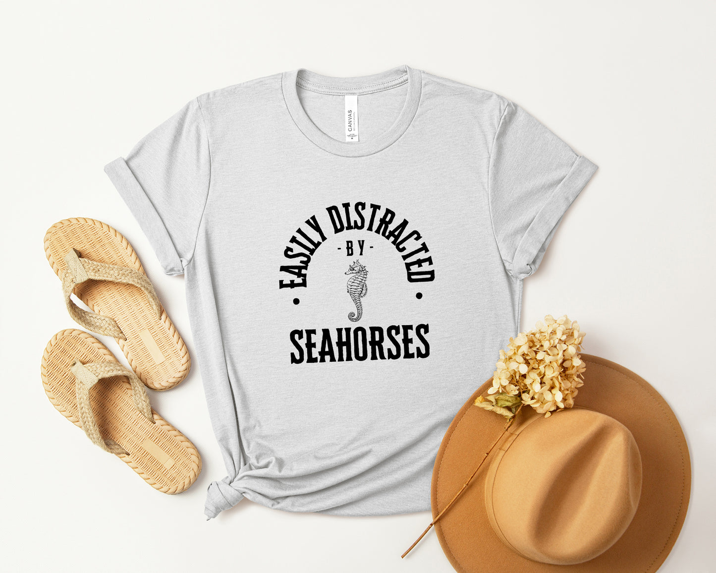 A vintage typeface t-shirt with a hand-drawn sketch of a seahorse and the caption "Easily Distracted by Seahorses." Perfect for seahorse lovers, marine biologists, and wildlife enthusiasts. Bella+Canvas 3001 t-shirt in ash. ReadyShirtAim.com