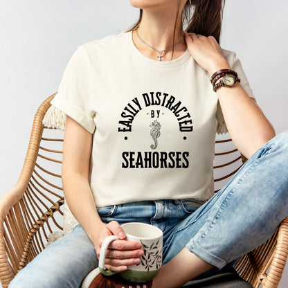 A vintage typeface t-shirt with a hand-drawn sketch of a seahorse and the caption "Easily Distracted by Seahorses." Perfect for seahorse lovers, marine biologists, and wildlife enthusiasts. Bella+Canvas 3001 t-shirt in natural. ReadyShirtAim.com