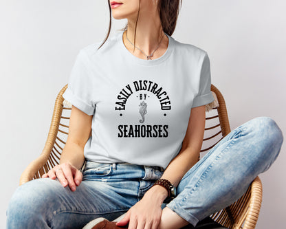 A vintage typeface t-shirt with a hand-drawn sketch of a seahorse and the caption "Easily Distracted by Seahorses." Perfect for seahorse lovers, marine biologists, and wildlife enthusiasts. Bella+Canvas 3001 t-shirt in silver. ReadyShirtAim.com