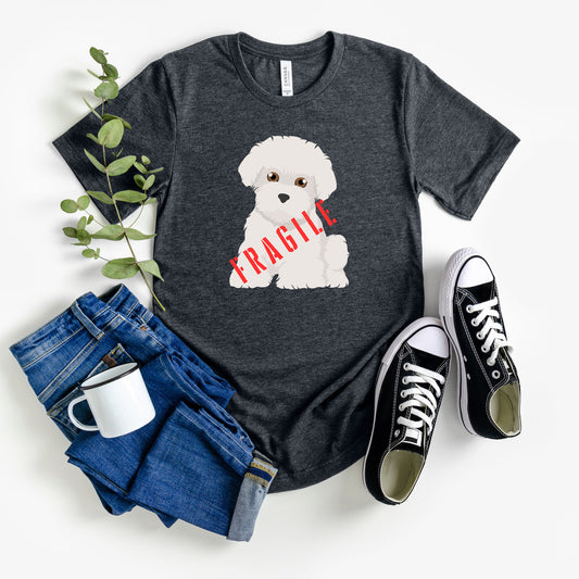 "Fragile" Maltese Dog T-Shirt for Unisex with a cartoon graphic of a Maltese dog sitting down and a bold red stenciled "FRAGILE" text overlay. Ideal for dog lovers with a quirky sense of humor. Bella+Canvas 3001 t-shirt in dark grey heather. ReadyShirtAim.com