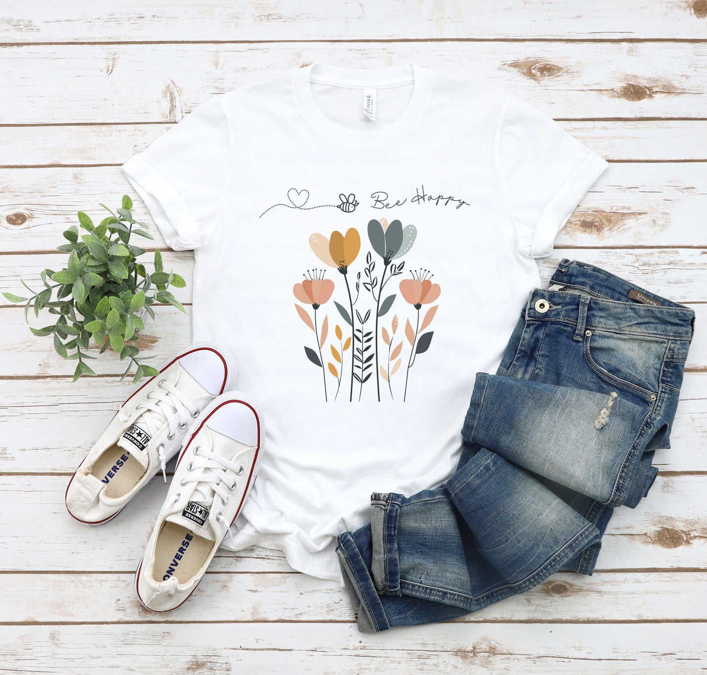 A Boho Scandinavian floral t-shirt with a simple flower design and the caption "Bee Happy." Perfect for spreading positive vibes, garden lovers, and nature enthusiasts. Bella+Canvas 3001 t-shirt in white. ReadyShirtAim.com