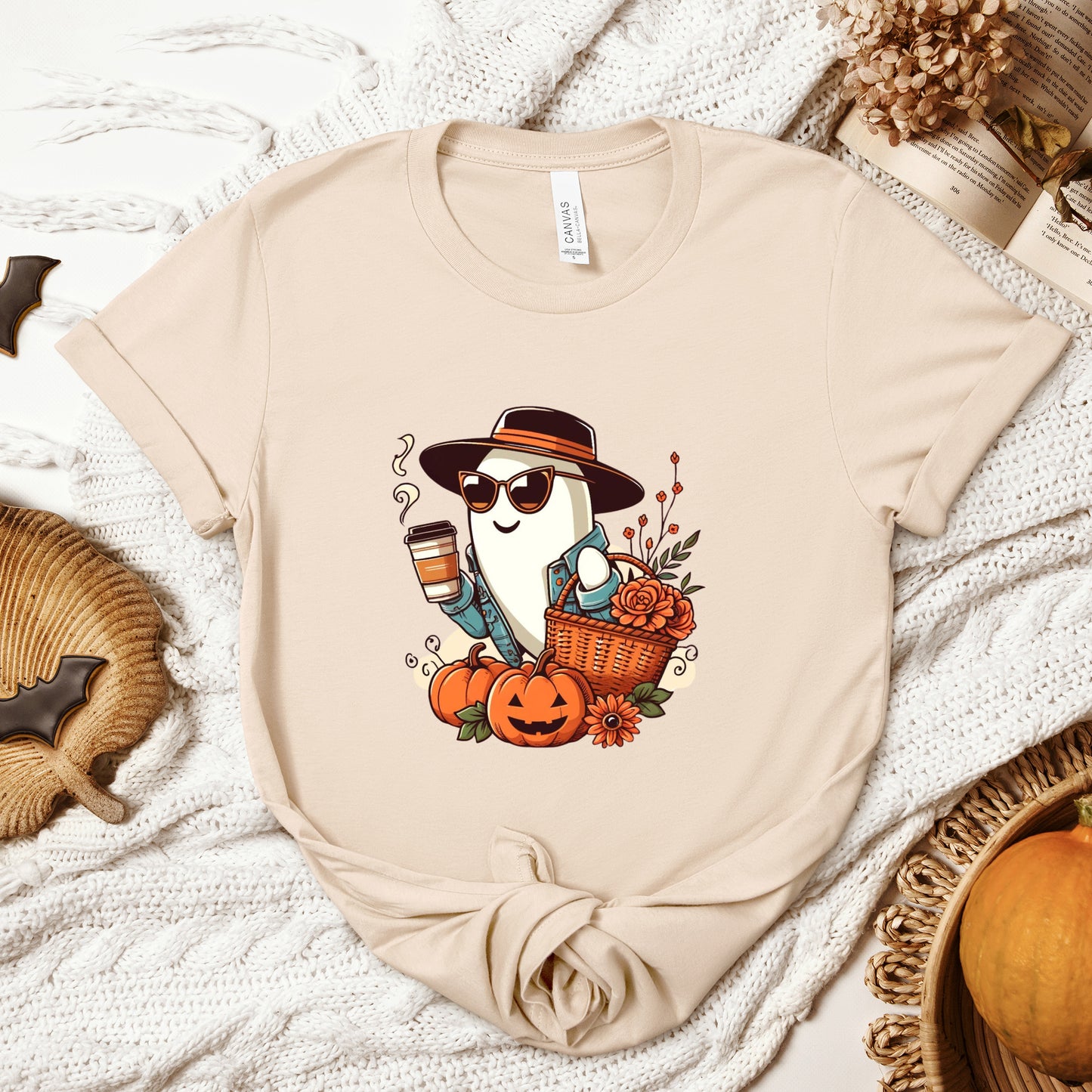 Fashionable Ghost Halloween T-Shirt for Women with a stylish ghost wearing cat-rimmed sunglasses, a jean jacket, and a wide-brimmed hat, carrying a Halloween basket and a café latte to-go cup, surrounded by flowers and Halloween elements.  Bella+Canvas 3001 t-shirt in soft cream. ReadyShirtAim.com