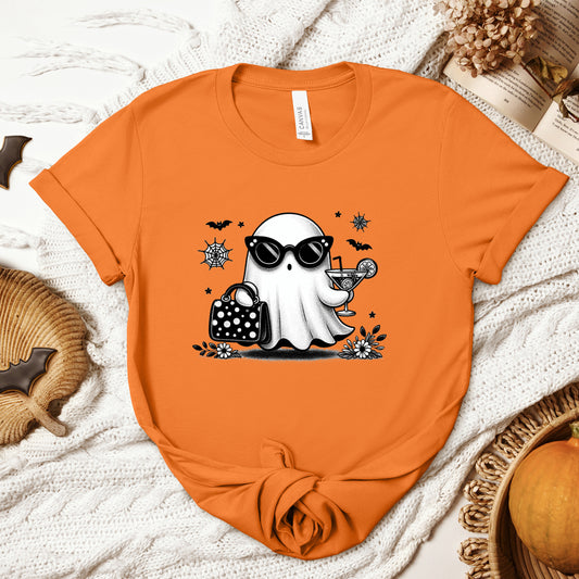 Fashionable Ghost Halloween T-Shirt for Women with a stylish ghost wearing cat-rimmed sunglasses, carrying a couture purse, and holding a cocktail, surrounded by flowers and Halloween elements. Bella+Canvas 3001 t-shirt in orange. ReadyShirtAim.com