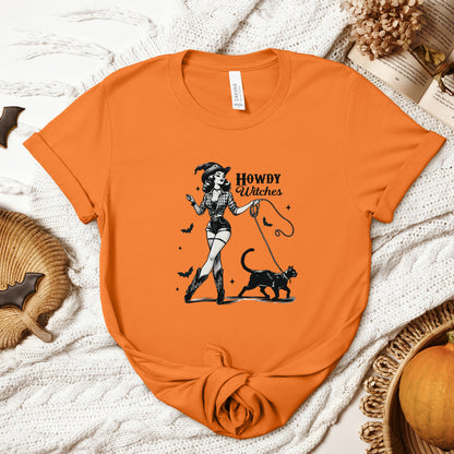 "Howdy Witches" Vintage 1950's Witch Halloween Women's T-Shirt featuring bold black text and a classic black-and-white image of a pin-up girl in sexy shorts and a western-style shirt, walking a black cat on a leash and smiling mischievously, perfect for adding a retro touch with playful Western charm to your Halloween festivities. Available in multiple colors and sizes.  Bella+Canvas 3001 t-shirt in orange. ReadyShirtAim.com