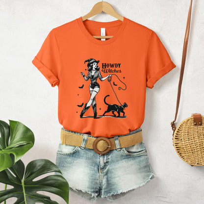 "Howdy Witches" Vintage 1950's Witch Halloween Women's T-Shirt featuring bold black text and a classic black-and-white image of a pin-up girl in sexy shorts and a western-style shirt, walking a black cat on a leash and smiling mischievously, perfect for adding a retro touch with playful Western charm to your Halloween festivities. Available in multiple colors and sizes.  Bella+Canvas 3001 t-shirt in orange. ReadyShirtAim.com