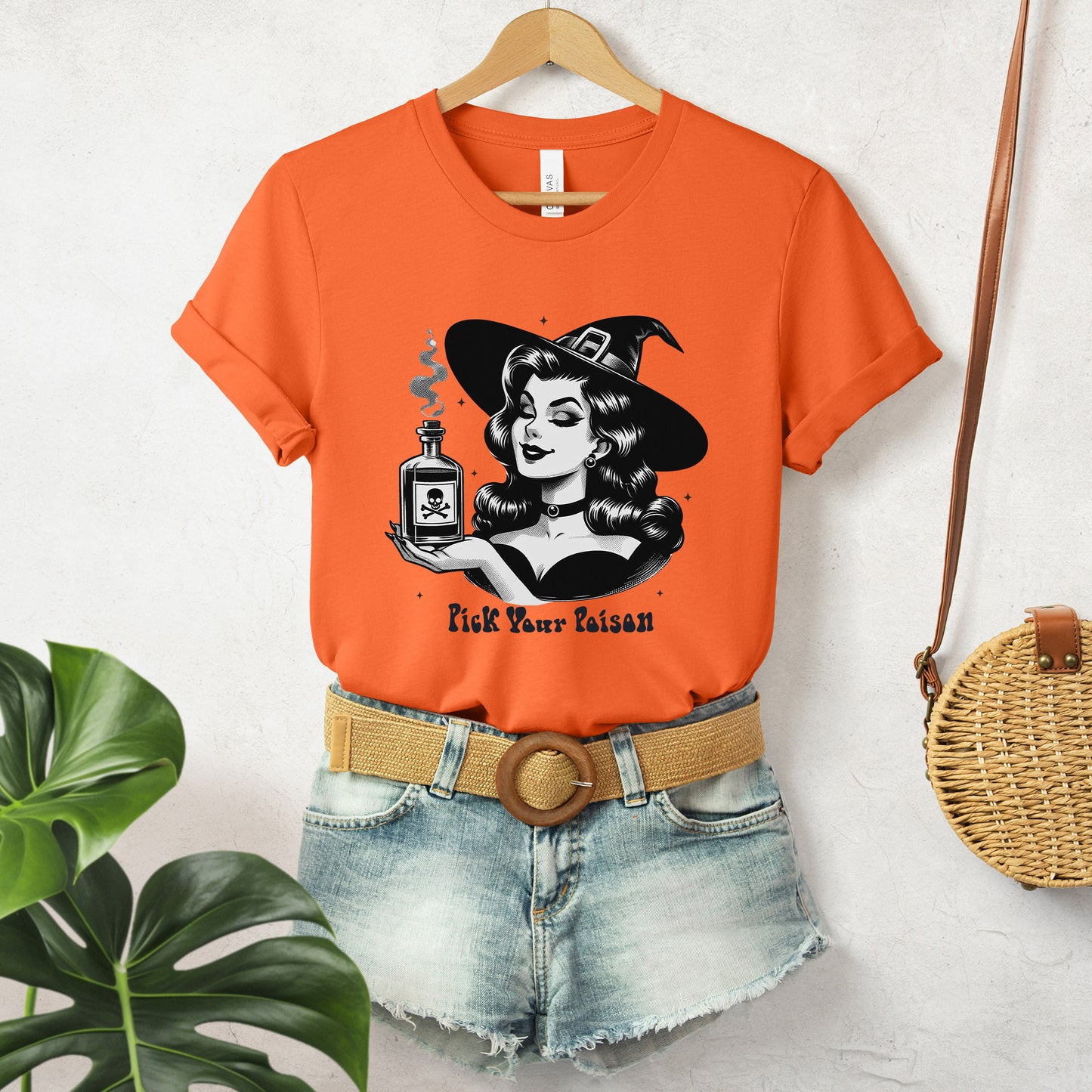 "Pick Your Poison" Vintage 1950's Witch Halloween Women's T-Shirt featuring bold black text and a classic black-and-white image of a pin-up girl in a sexy witch costume, gazing at a large, steaming potion bottle with a skull and crossbones on it, perfect for adding a retro touch with mystical charm to your Halloween festivities. Available in multiple colors and sizes.  Bella+Canvas 3001 t-shirt in orange. ReadyShirtAim.com